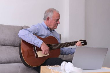 Kulaklıklı yetişkin bir adam evde dizüstü bilgisayarla gitar çalmayı öğreniyor. Covid19 salgınında kavramsal öğrenme.