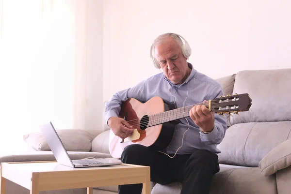 Kulaklıklı yetişkin bir adam evde dizüstü bilgisayarla gitar çalmayı öğreniyor. Covid19 salgınında kavramsal öğrenme.