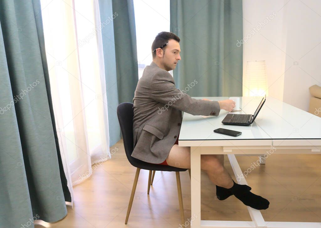 Sophisticated man in blazer and red underwear working from home laying mug down