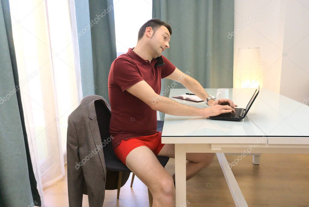 Sophisticated man in red underwear working from home talking by phone and using computer