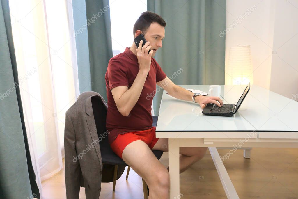 Sophisticated man in red underwear working from home talking by phone and using computer