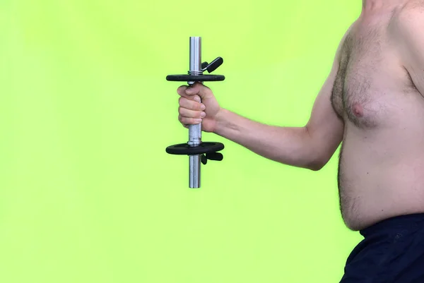 Arm of a middle-aged fat man in his 30s lifting a dumbbell weight to get fit. Concept fitness and weigh reduction. Green background.