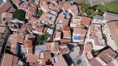 Bu sahnede yeşilliklerle çevrili kırmızı kiremitli çatıları olan büyüleyici bir köy var. Evlerin arasında dar sokaklar örülüyor, Akdeniz kasabalarının tipik barışçıl atmosferini yaratıyor..