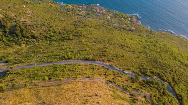 Okyanus manzaralı sahil şeridi boyunca kıvrımlı yol ve günbatımında yeşil tepeler