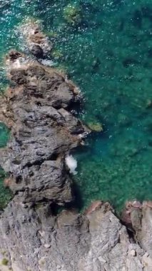 Güneşli bir günde Açık Mavi Okyanus 'un yanındaki bir sahil noktasında kayalara vuran dalgalar.