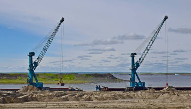 İki Liebherr turnası Dudinka limanındaki mavnalardan kum boşaltıyor.