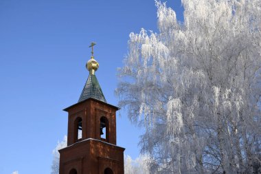 Kışın Vaftizci Aziz John Kilisesi 'nin çan kulesi mavi gökyüzüne ve Tyukalinsk şehrindeki don kaplı ağaçlara karşı Rusya Omsk bölgesinde