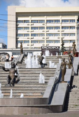 Yenisei, Khatanga, Angara, Mana, Bazaiha nehirlerini çevreleyen binaların arka planında tasvir eden heykellerle Krasnoyarsk şehir merkezindeki çağlayan çeşmenin fotoğrafı