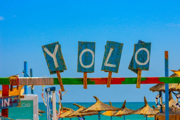 YOLO - you only live once - sign on wooden boards at entrance to beach bar close to the Black Sea on a sunny day