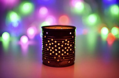 Yanan bir mumu olan metal bir şamdan ve renkli ışıkların arka planına karşı kalp şeklinde bir desen. Bulanık, belirsiz bir geçmiş. Bokeh.