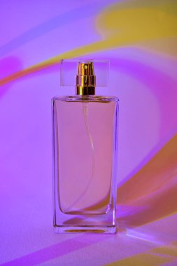 Çok renkli neon şeritlerin arka planında parfüm bulunan cam şişe. Yakın çekim, soyut. 