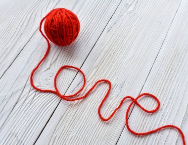 Örgü örmek için kırmızı iplik yumağı. Aşk sözcüğü örgü ipliğinden yapılır. Beyaz tahta arkaplan.