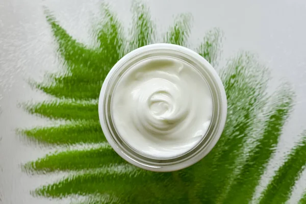 Texture of natural, bio, cosmetic body or face cream on glass with green leaf. Close-up.