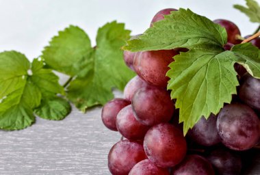 Gri ahşap zemin üzerinde kırmızı, taze, olgun üzümler ve yeşil asma yaprakları. Yakın plan..