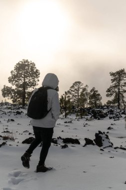 Beyaz ceketli genç ve kar içinde sırt çantalı.