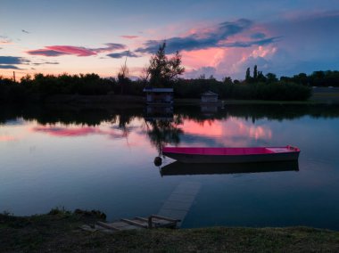 Yazın Sava nehrinin manzarası, batık ahşap rıhtımlı demirli pembe bir tekne ve ufkun üzerinde büyük pembe bir kümülonimbus bulutu, akşam üzeri renkli günbatımında..