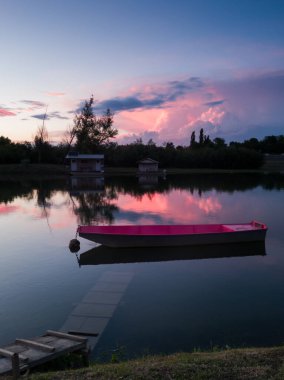 Yazın Sava nehrinin manzarası, batık ahşap rıhtımlı demirlemiş bir tekne ve ufkun üzerinde büyük bir kümülonimbus bulutu akşam üzeri renkli günbatımında..