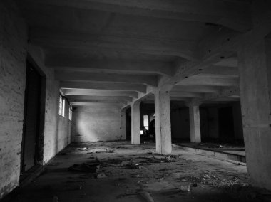 Terk edilmiş bir beton binanın içinde küçük pencereleri ve büyük kapıları olan eski bir endüstriyel depo var..