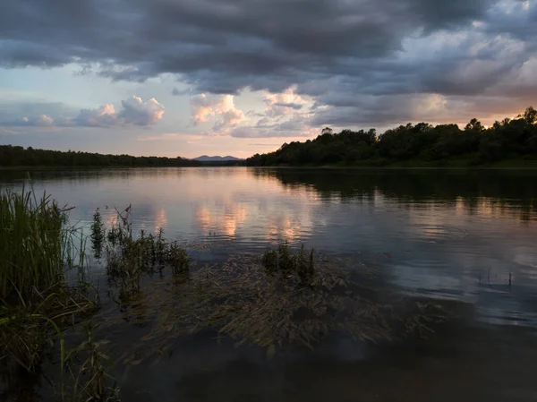Krajobraz Rzeką Ciemne Chmury Wysoka Trawa Wodna Góra Oddali Zachodzie — Zdjęcie stockowe
