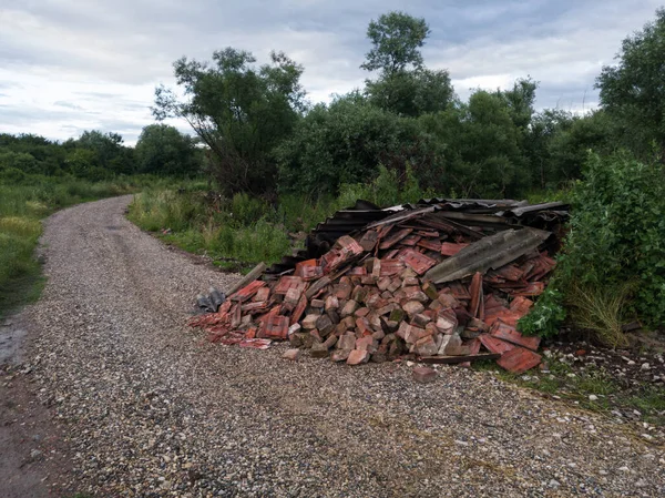 Çakıl yolu, orman, bulutlu gökyüzü ve moloz ve asbest tabakalı çöp yığını, ekolojik etki, inşaat malzemeleri, doğa kirliliği, vahşi atık alanı, endüstriyel atıklar