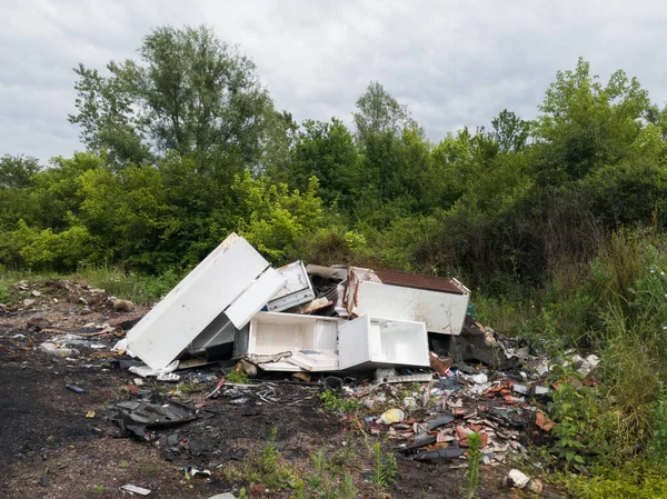 Beyaz eşyalar, çöplük, çöp kundaklama, negatif ekolojik etki, ekosistem hasarı, doğanın ihmali, bulutlu bir günde yeşil ağaçlı arazide zehirli atıklar.