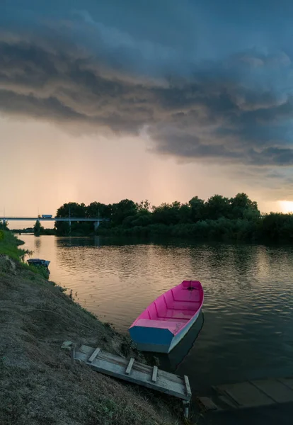 Şiddetli yağış veya yaz yağmuru, şiddetli hava ve yağmurun ardında parlayan güneş fırtınası ve kümülonimbus bulutu. Fırtınalı bir akşamda Sava nehri ile ahşap rıhtımın yanında demirli bir tekne manzarası