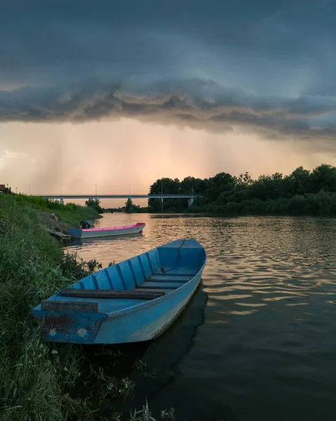 Şiddetli yağış veya yaz yağmuru, şiddetli hava ve yağmurun ardında parlayan güneş fırtınası ve kümülonimbus bulutu. Çimenli nehir kıyısı ve köprü boyunca demirli teknelerle Sava nehri manzarası.