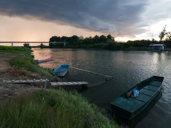 Şiddetli yağış veya yaz yağmuru, şiddetli hava ve yağmurun ardında parlayan güneş fırtınası ve kümülonimbus bulutu. Tahta rıhtım ve köprünün yanında demirli teknelerle Sava nehri manzarası