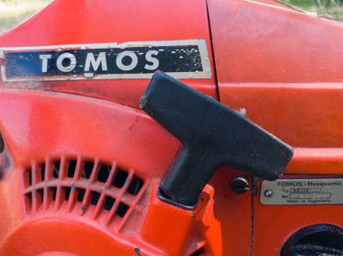 Biraz talaş kaplı eski kırmızı Tomos-Husqvarna benzin testeresini çekmeye başla.