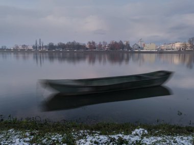 Kışın alacakaranlıkta uzun süre suda demirli kalan tekne, sakin yansıyan su ve nehir kıyısındaki çimenler karla kaplıydı.