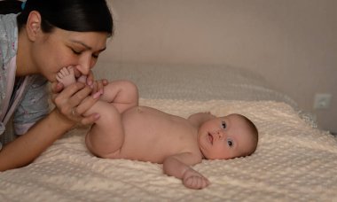 Anne, yeni doğan şirin bebeğin ayak parmaklarını kesiyor. 6 haftalık bebek yatakta yatıyor. Anneyle bebek. Seçici odak. 