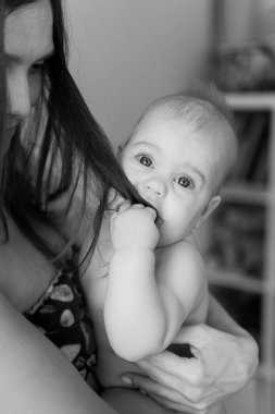 Tek renkli esmer kadın portresi bebeğini kollarında sıkıca tutuyor. Bebek çekme ve anne saçıyla oynama. Seçici odaklanma. Siyah ve beyaz.