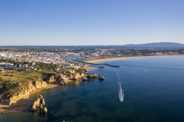 Gün doğumunda Camilo Sahili 'nde. Lagos, Algarve, Portekiz. Portekiz 'in güneyindeki altın sahil kayalıkları. Güneşli bir hava manzarası. Turkuaz deniz. Tekne.