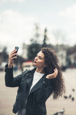 Çekici kıvırcık saç stili koyu tenli birinin portresi telefonda konuşuyor dişlek gülüşlü, haftasonu boş zamanlarında dışarıda yürüyor.