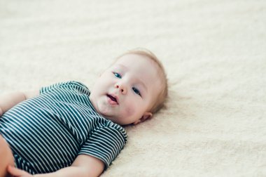 Çocuk yatakta oynuyor, gülümsüyor.