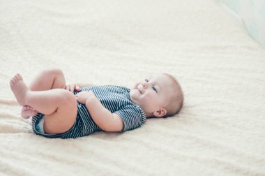 Çocuk yatakta oynuyor, gülümsüyor.