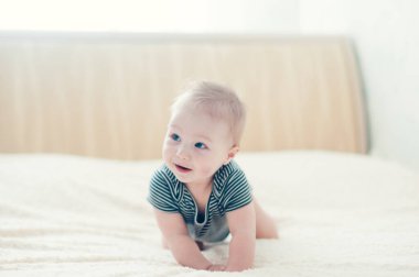 Çocuk yatakta oynuyor, gülümsüyor.