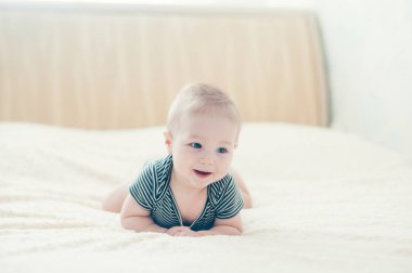 Çocuk yatakta oynuyor, gülümsüyor.