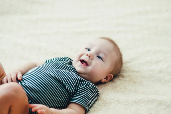 Çocuk yatakta oynuyor, gülümsüyor.