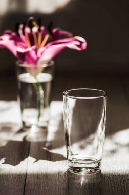 Ahşap zemine yerleştirilmiş cam soğuk su. Zambak çiçekleri..