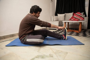 Asyalı Hintli adam oyun oynuyor, canlı yayın yapıyor ve TV seyrediyor. Oturma odasında, gri bir kanepe ve beyaz bir masa üzerinde..