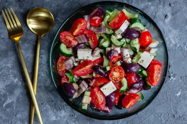 Altın çatal bıçaklı gri yüzeyde Yunan salatası.