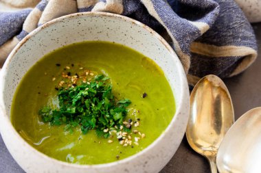Beyaz seramik malzemeli yeşil çorba, peçeteler, kaşık, gri bir yüzey üzerinde ekmek dilimleri.