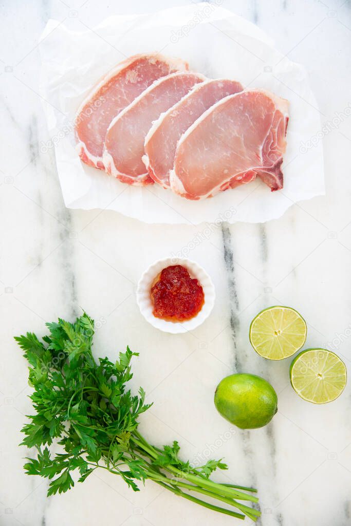 Raw pork chops, sweet chilli sauce,  lime, parsley leaves, food knolling.