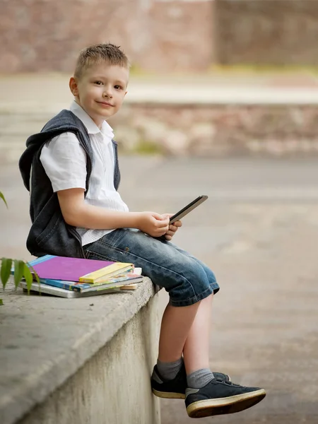smile boy near school with a tablet and a book cums outside the school on the street and waits for lessons