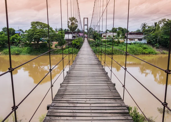 Puente colgante de cuerda sobre un río en inundación al atardecer, Tailandia — Foto de Stock