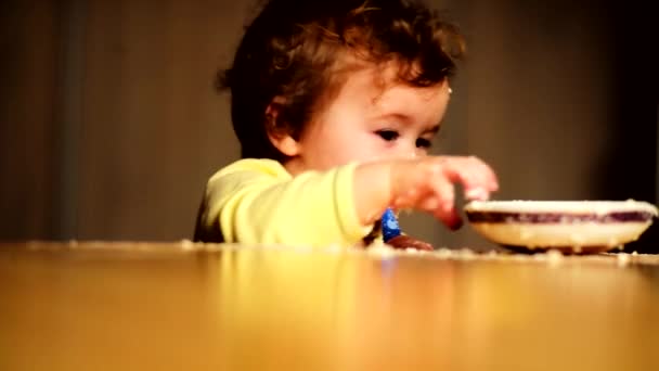 Petit bébé bouclé avec les premières dents mâcher sur une cuillère à la table du dîner — Video