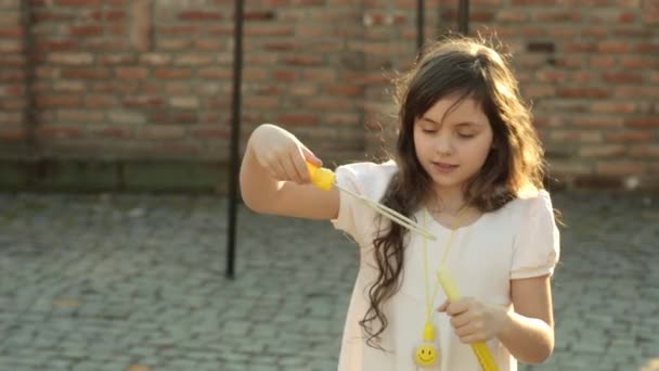 Roztomilá holčička v bílých šatech s mýdlovými bublinami na pozadí cihlovou zeď na zahradě — Stock video