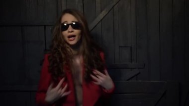 seksi esmer kadın güneş gözlüğü ve çıplak bir vücut üzerinde kırmızı bir ceket rap şarkı söylüyor.