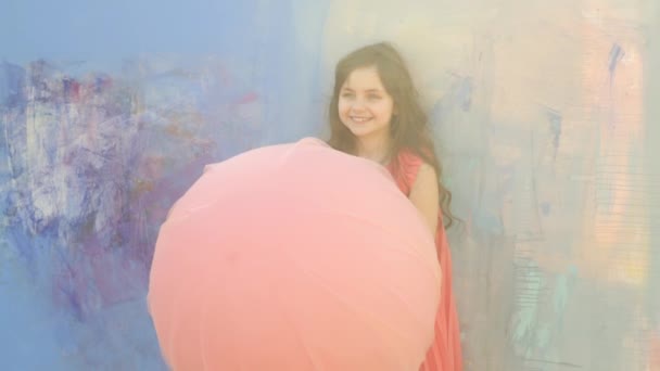 Schöne Teenie-Mädchen in orangefarbenem Kleid mit rosa Ballon auf blauem Hintergrund — Stockvideo